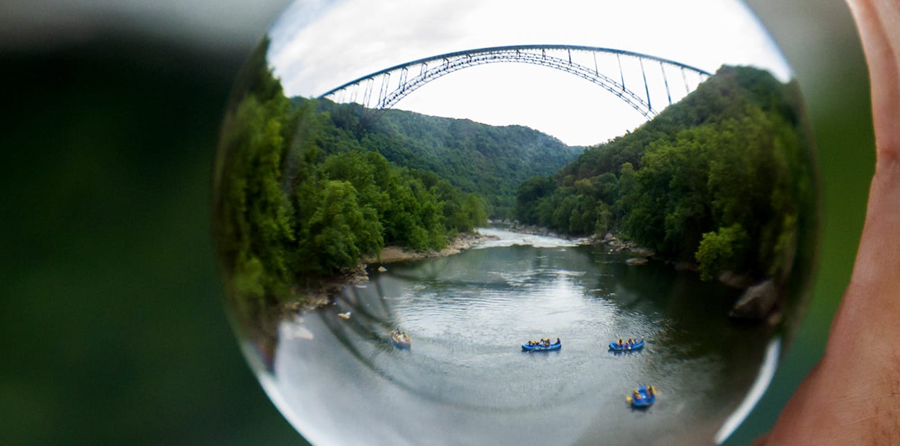 Rafts pass under the New River Gorge Bridge, the best known landmark of west virginia whitewater rafting.