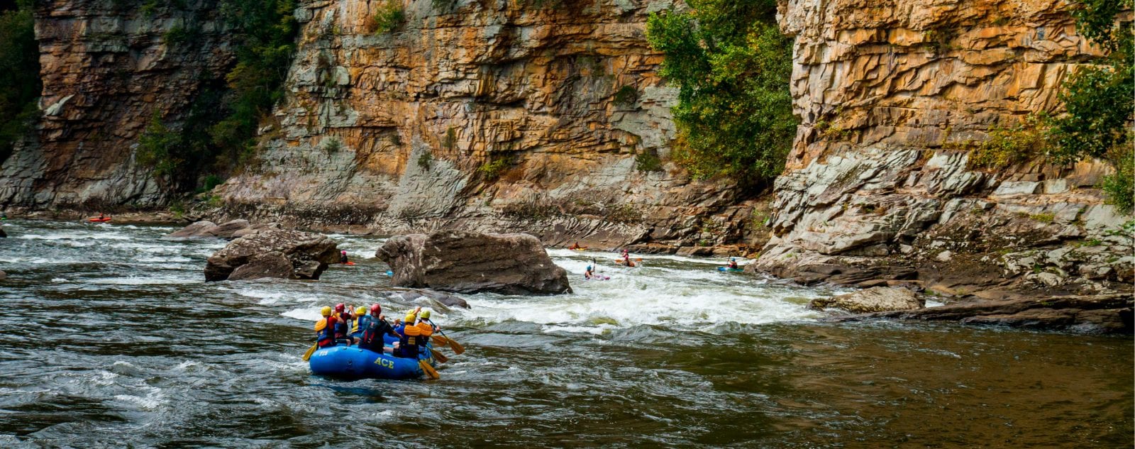 A raft enters cliffside rapid next to scenic cliff walls on a Lower Gauley River rafting trip.