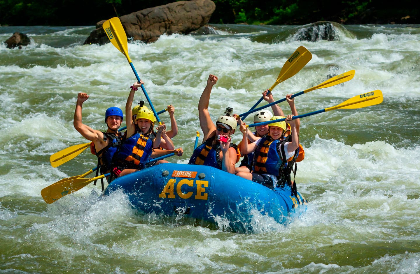 A family smiles and cheers on their lower new river gorge rafting trip while running fayette station rapid.