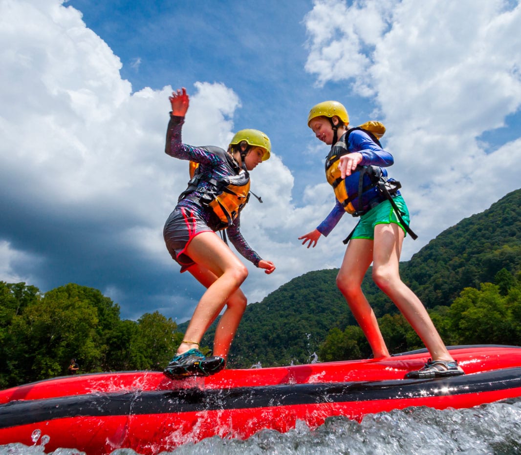 Two young girls play on top of an inflatable kayak on an upper new river gorge trips during summer rafting season.