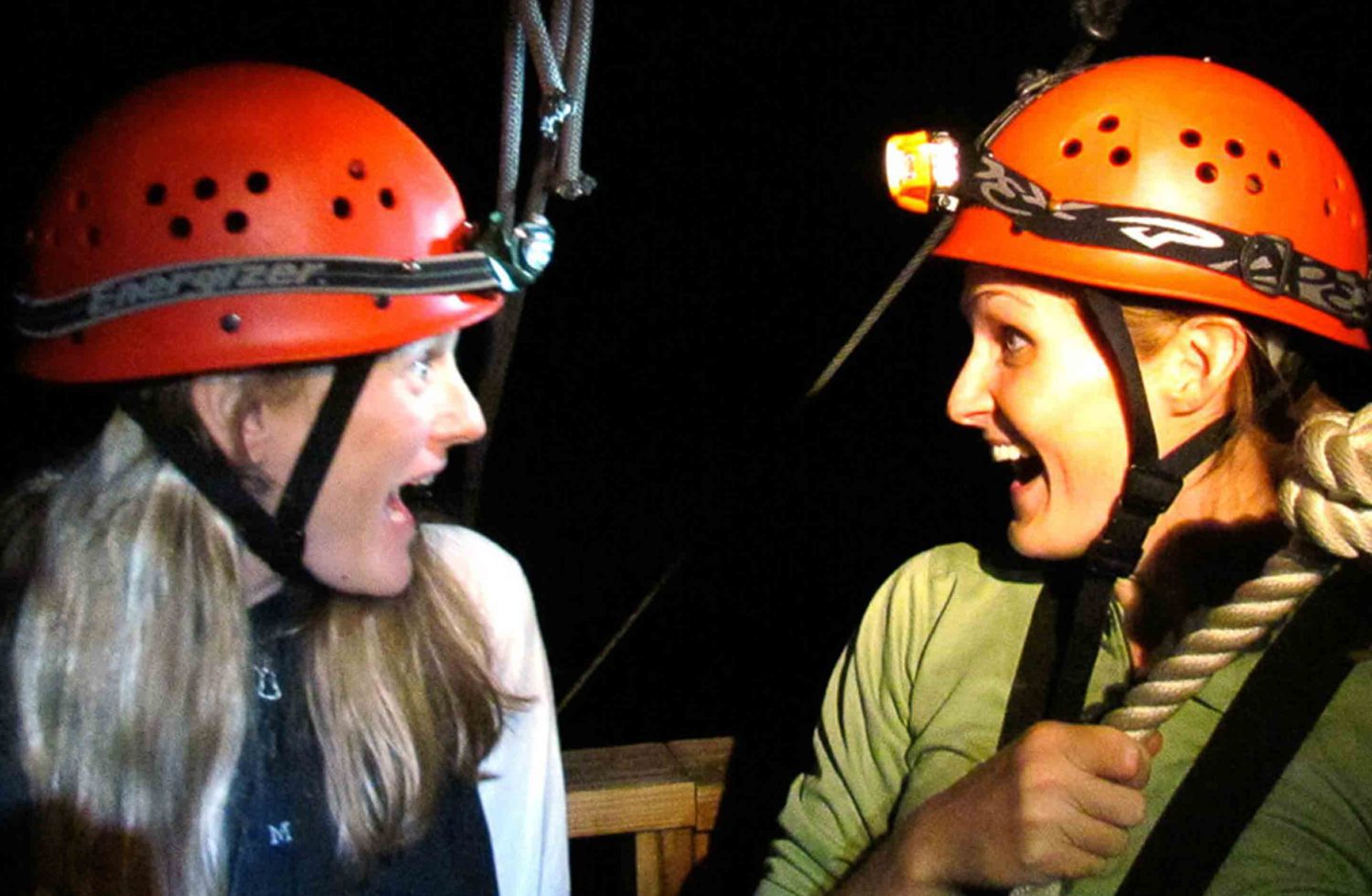 Friends look at each other before taking off from the platform on a night time zip trip.