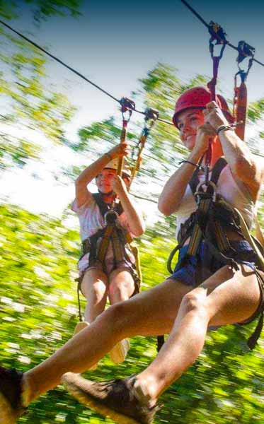 Two young women zipline beside each other at ace adventure resort in the new river gorge national park.