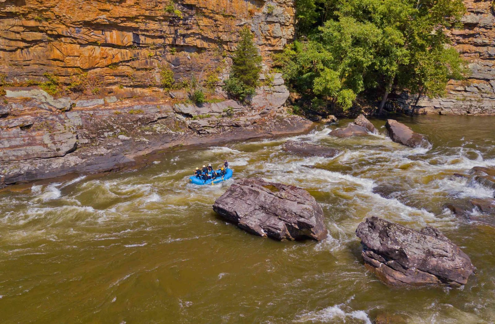 A raft passes giant scenic sandstone cliffs on a gauley river rafting trip in West Virginia.