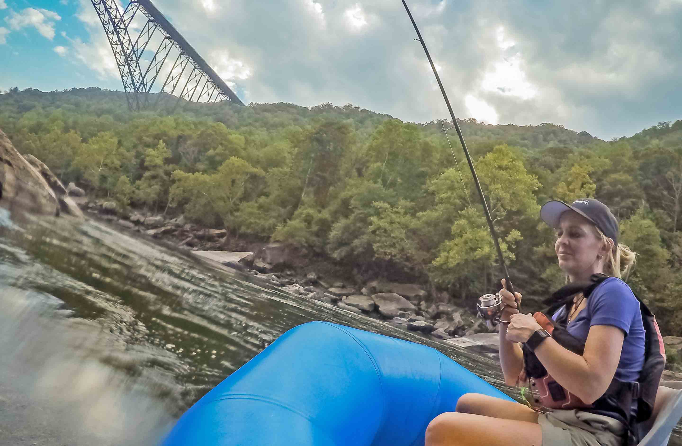 A woman reels in a fish while fishing on a guided tour with ACE Adventure Resort under the New River Gorge Bridge.