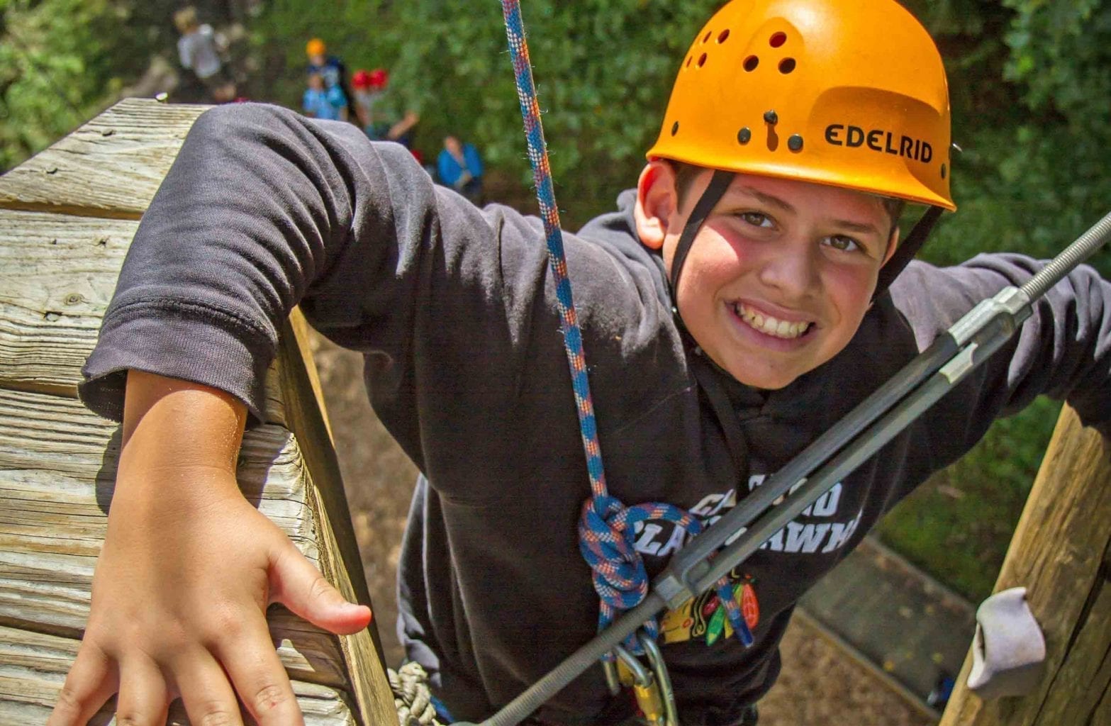 A kid smiles and makes his way up the climbing tower on the Team Challenge Course at ACE Adventure Resort in Southern West Virginia.