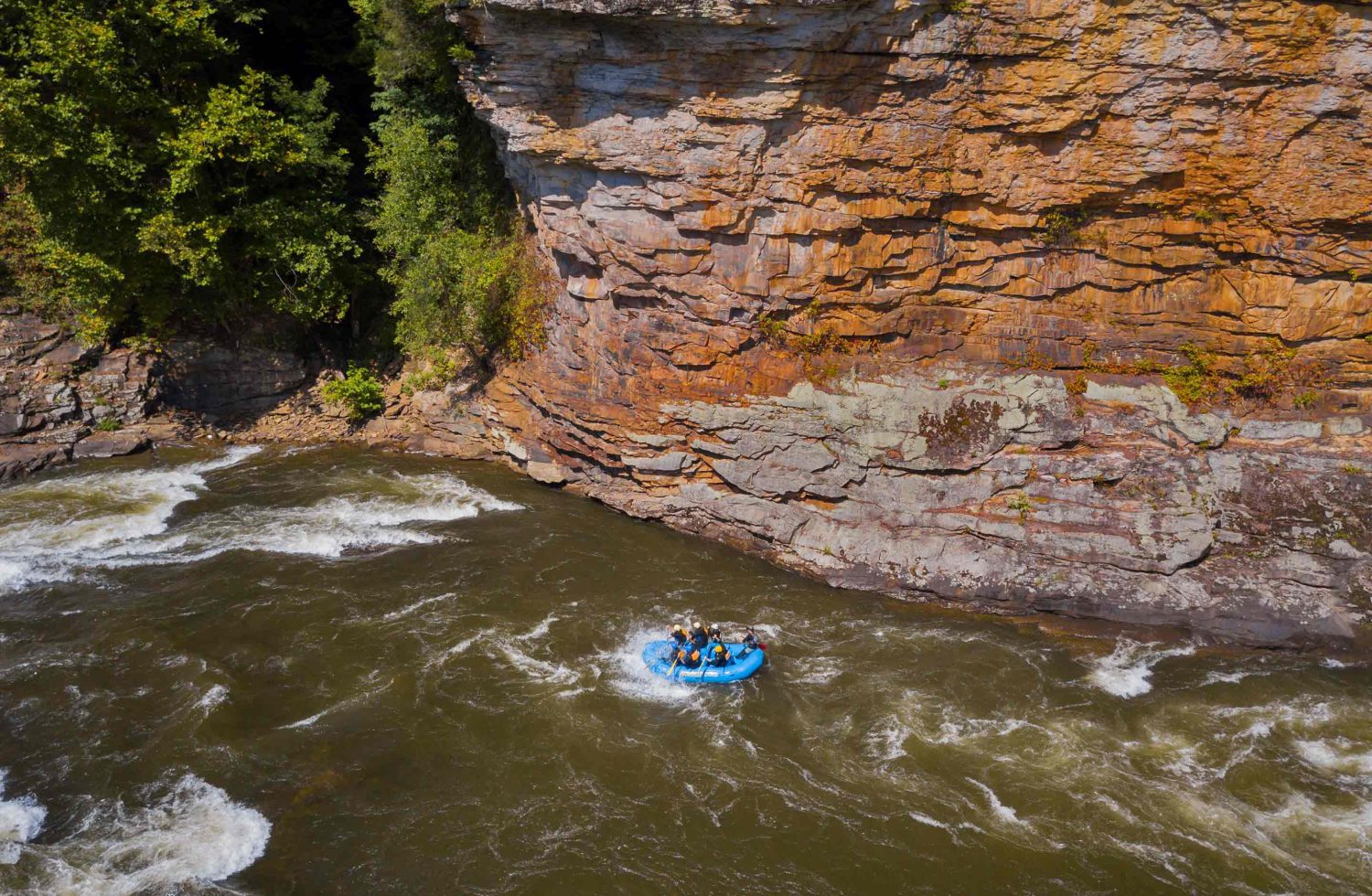 A raft passes the giant, sandstone cliffs of cliffside rapid on the Lower Gauley River.