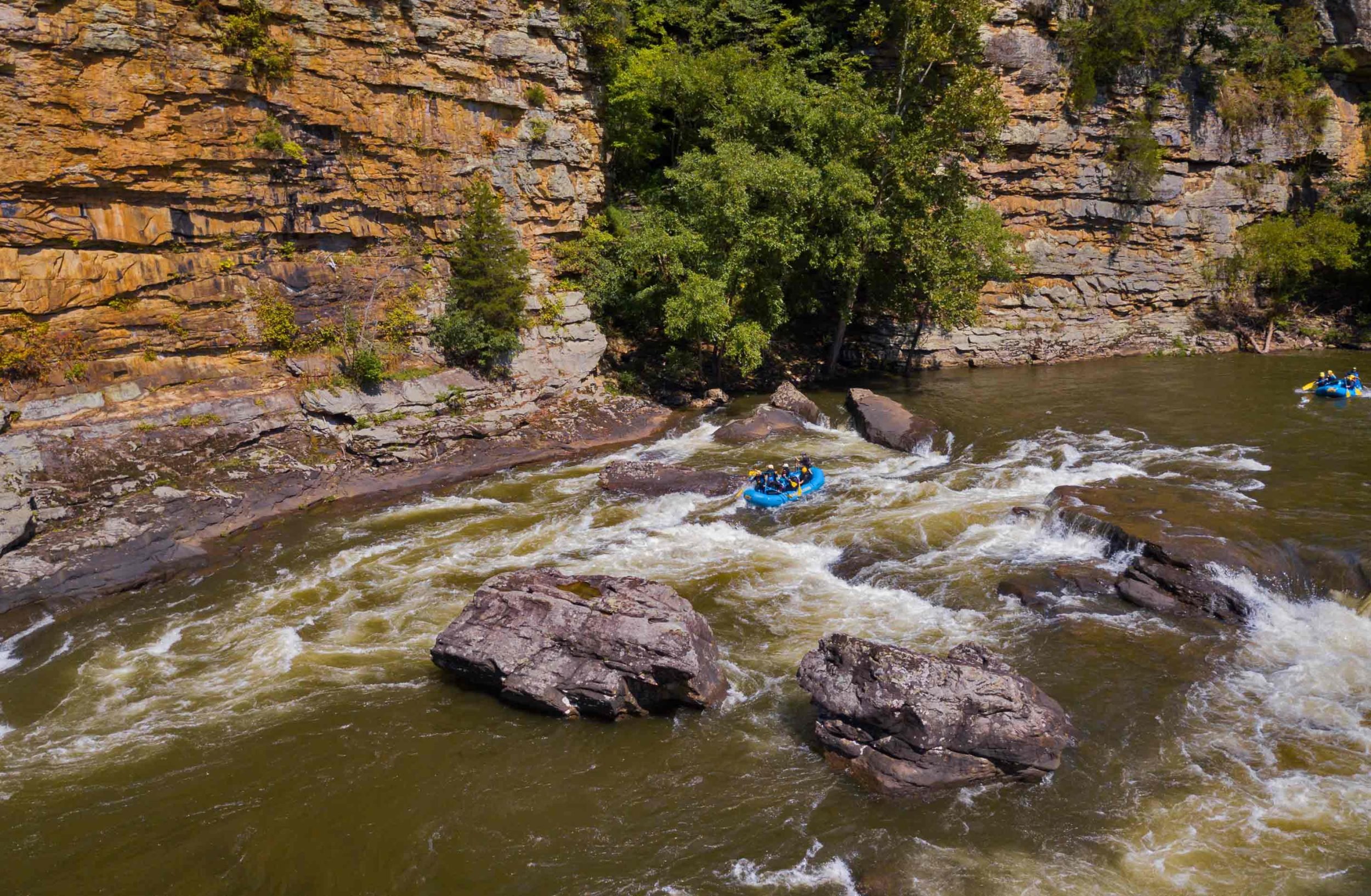 An aerial view of an ACE raft passing soaring sandstone cliffs while on a lower gauley rafting trip in west virginia.