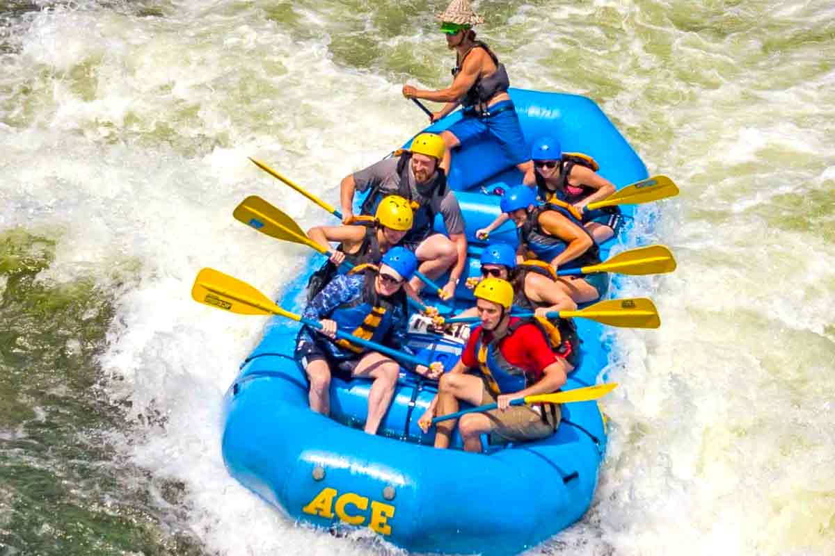 A boat of smiling people surfs on a wave hole during a New River Gorge white water rafting trip in West Virginia with ACE Adventure Resort