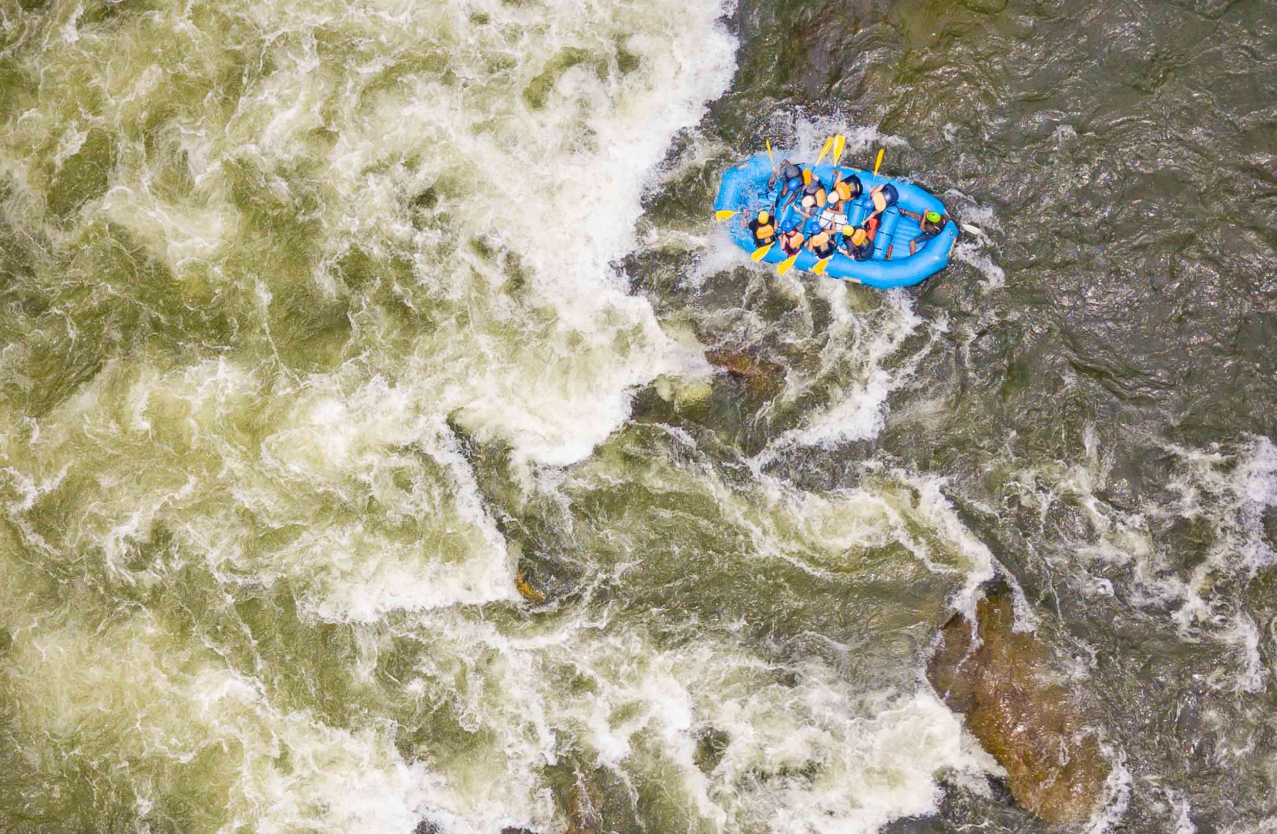 A drone shote of a small blue raft running a giant rapid on a New River Gorge white water rafting trip in West Virginia.