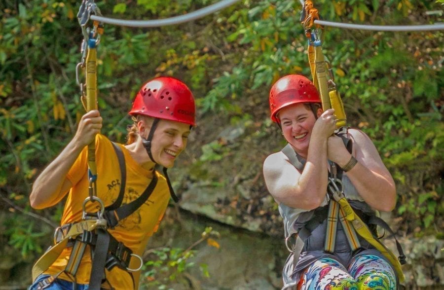 Two friends zip side by side on parallel double zip lines on the zip line canopy tour at ACE Adventure Resort.