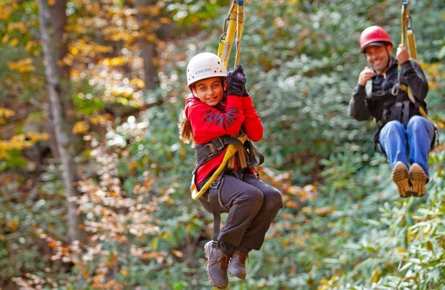 A father and daughter zip line together in tandem on the fall zip line course at ACE Adventure Resort in the New River Gorge.