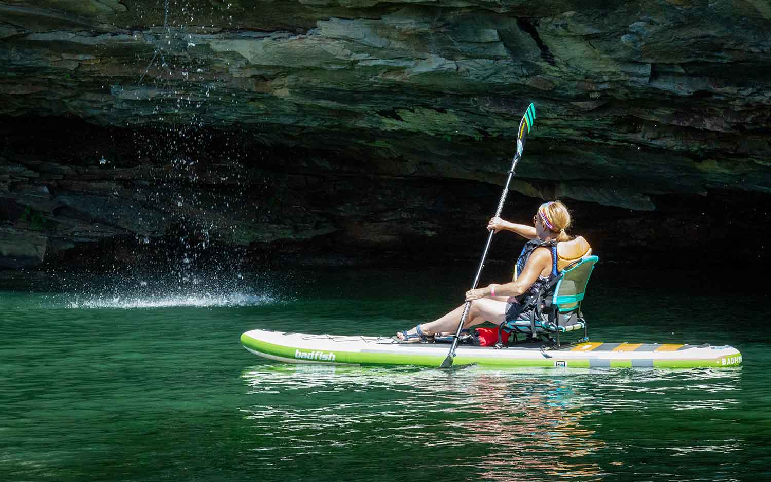 A guest enjoys kayak touring on summersville lake in west virginia beneath a waterfall with ace adenture resort.