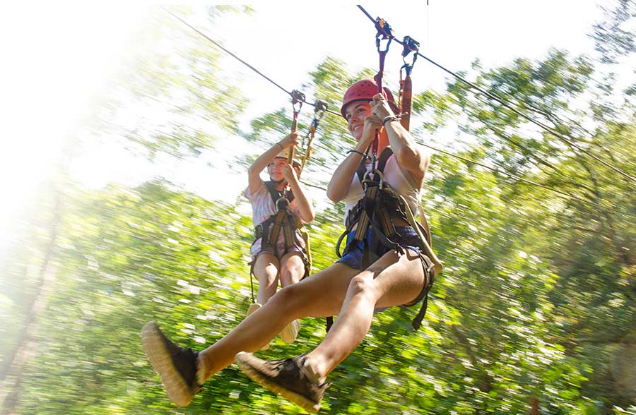 Two smiling women fly through the treetops on a new river gorge national park zip line canopy tour at ACE Adventure Resort