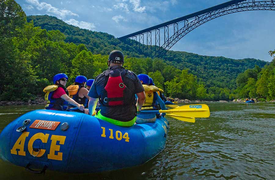 A raft full of guests paddle under the new river gorge bridge on a whitewater rafting trip.